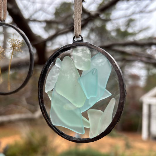 Round glass ornament with sea glass pieces hanging outdoors.
