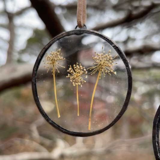 Decorative ornament with dried plants inside a circular frame against a blurred natural background